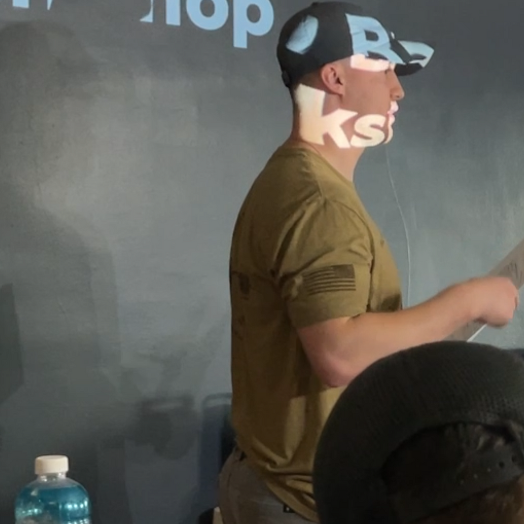 Person wearing a cap with text, standing in front of a screen with projected text.